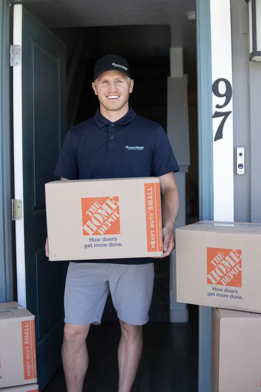 Utah's Moving & Storage crew member in branded polo carrying a moving box at a customer's front door